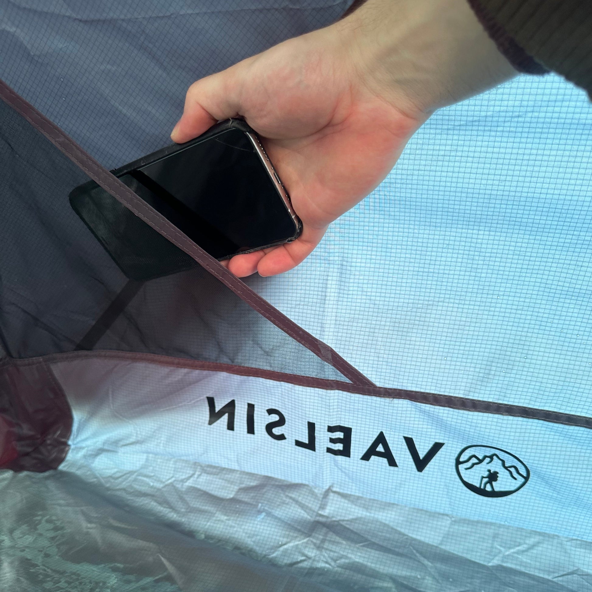 Person holding a phone next to a tent with 'Vaelsin' branding.