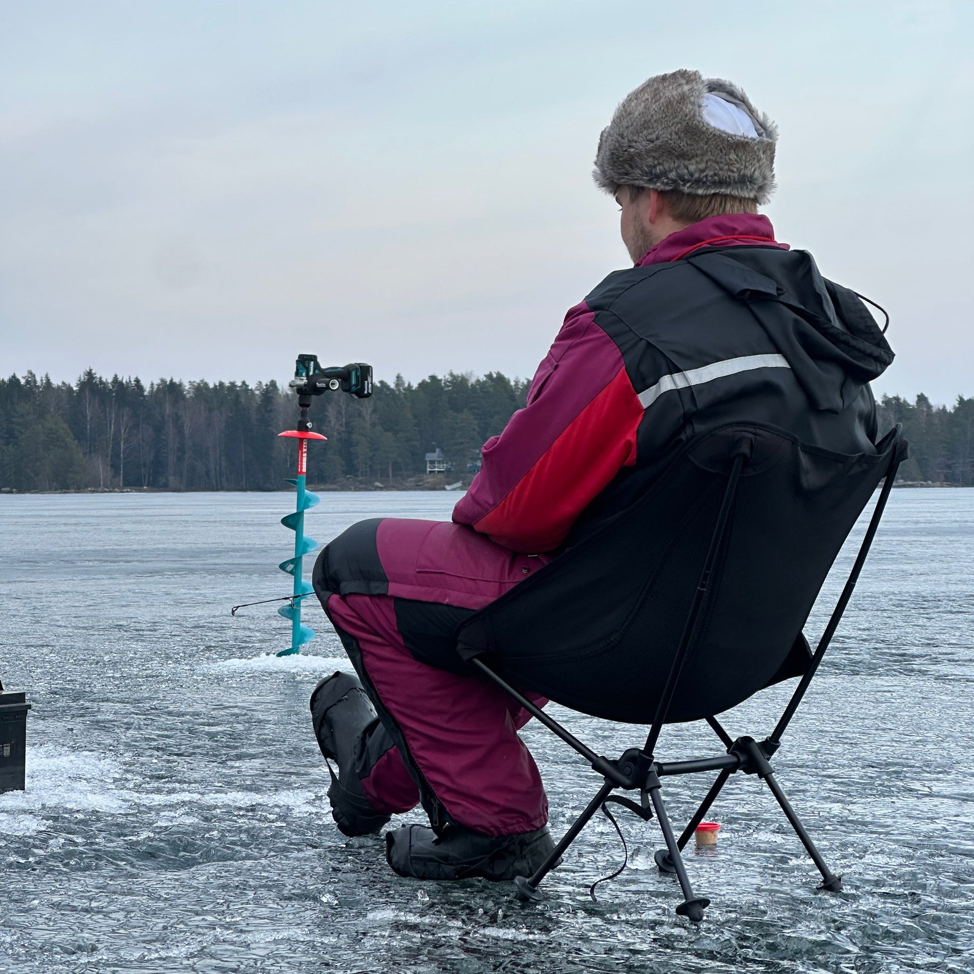 Person ice fishing on a frozen lake wearing winter clothing.
